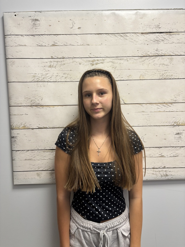 A student posing for a photo in front of a wooden wallpaper.