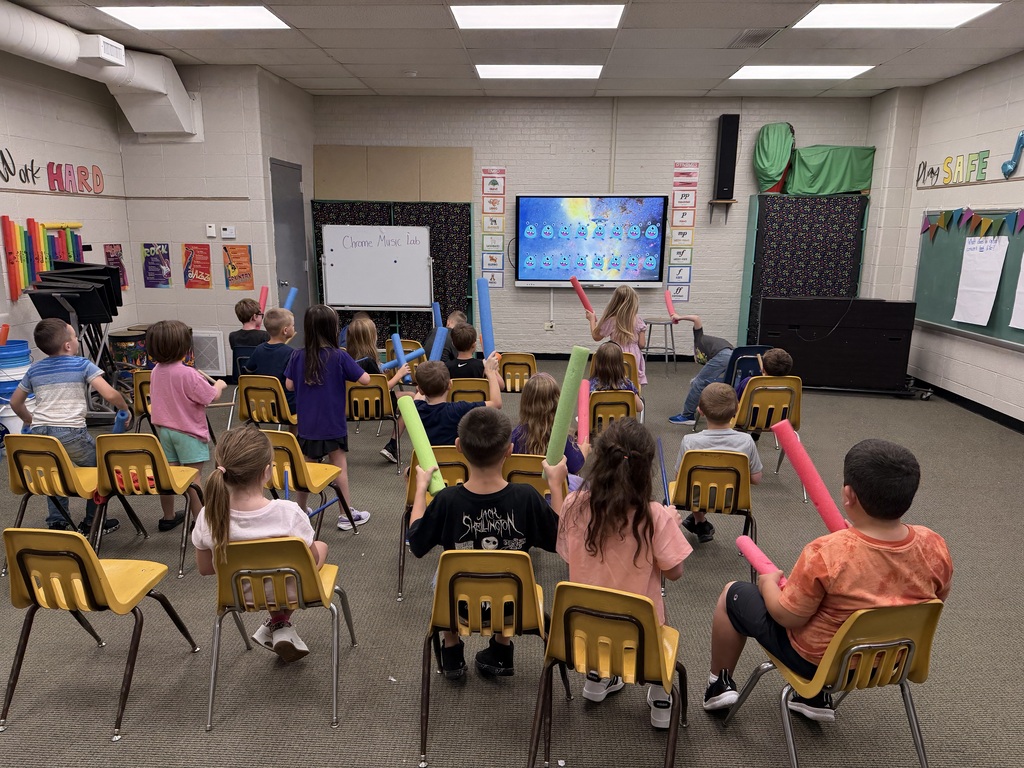 A group of students playing with pool noodles in a music classroom.