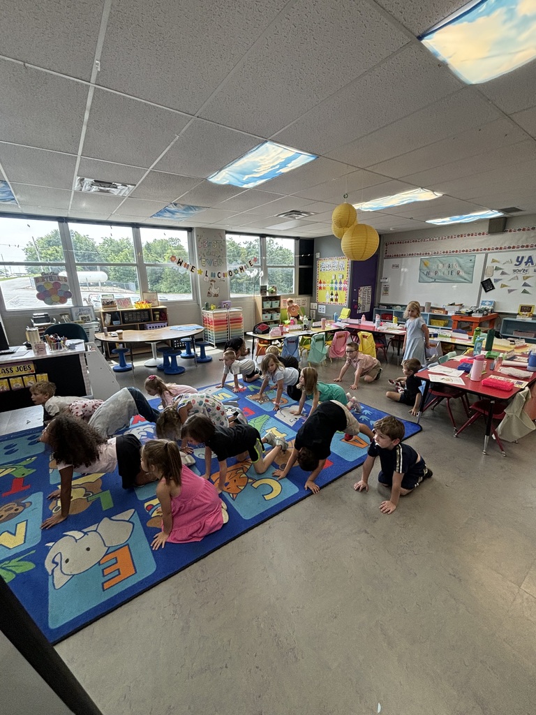 A classroom of young students doing yoga on a school rug.