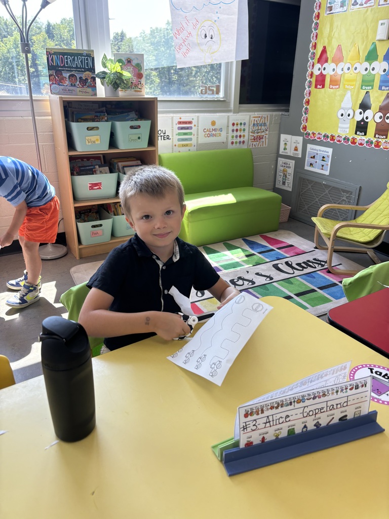 A young student cutting a piece of paper in a school classroom.