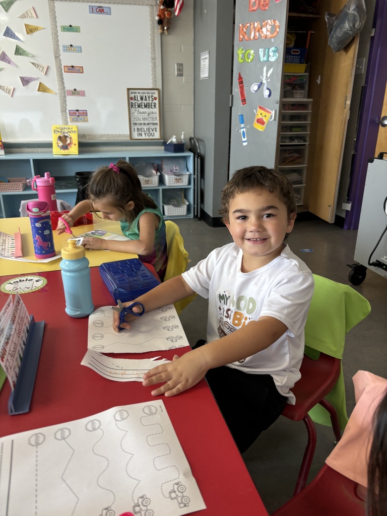 A young student cutting a piece of paper in a school classroom.
