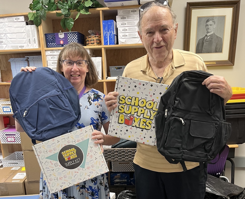 Two adults holding school backpacks and school supply boxes.