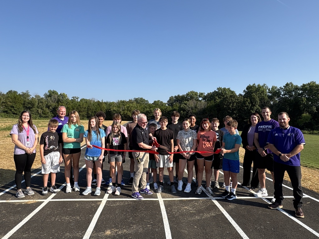 Students and staff gather on a new outdoor track as a staff member prepares to cut a red ribbon.