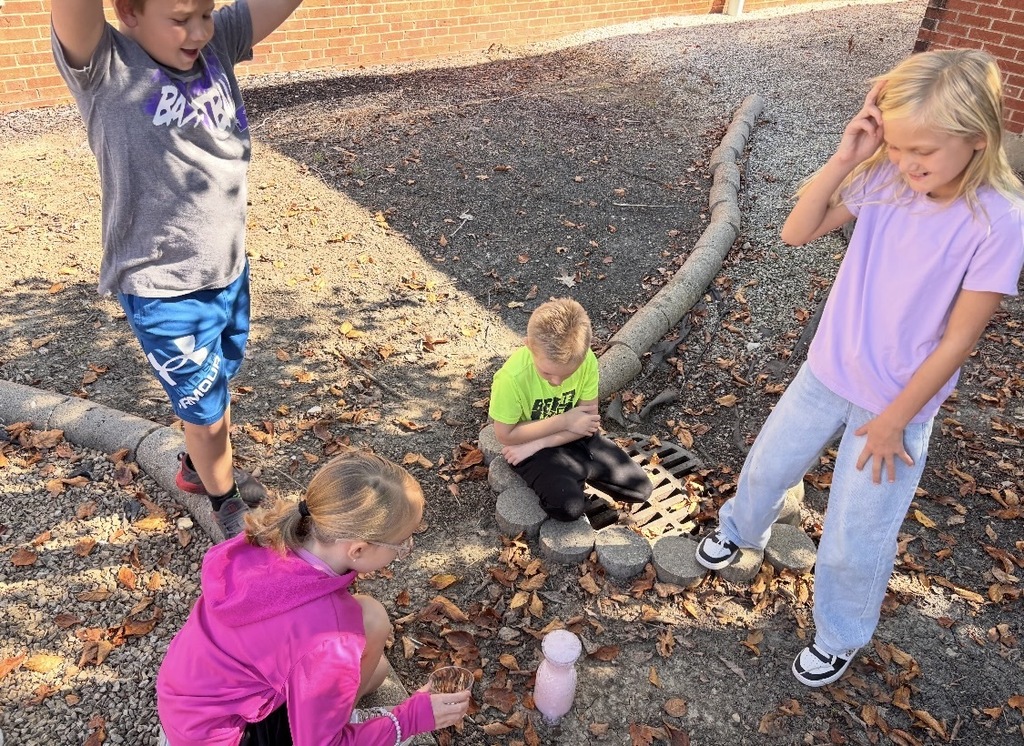 Four students gather excitedly around a bubbling pink science experiment during an outdoor activity.