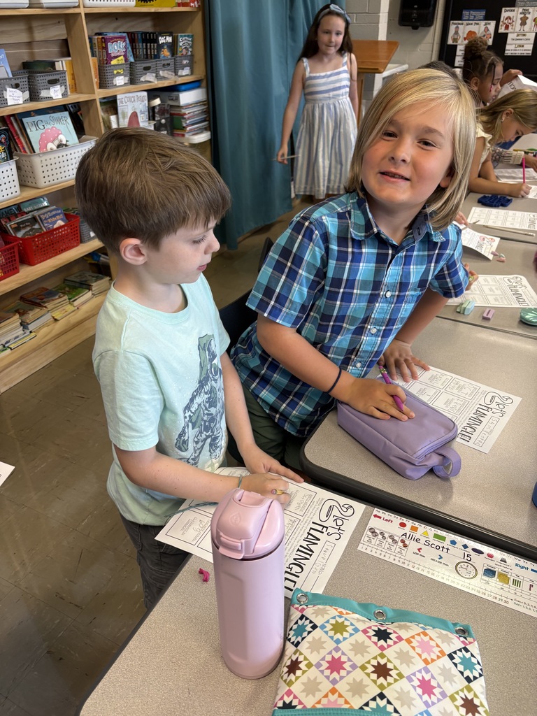 Two students stand at classroom desks with โLetโs Flamingleโ worksheets while classmates work nearby.