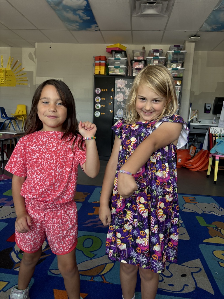 Two students smile and show off colorful beaded bracelets they made in their classroom.