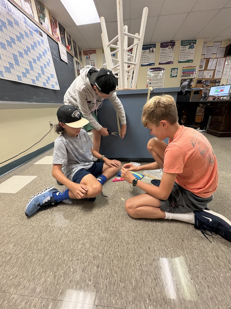 Three students collaborate on a hands-on classroom activity while seated together on the floor.