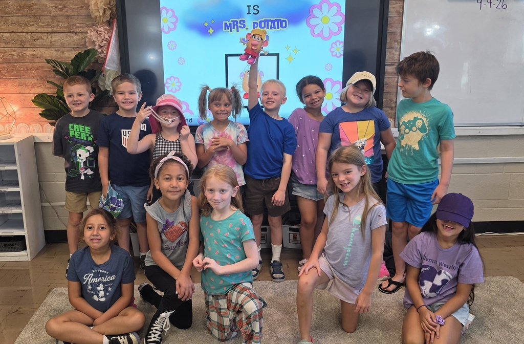Students pose together in a classroom, smiling and wearing playful accessories inspired by Mrs. Potato Head.