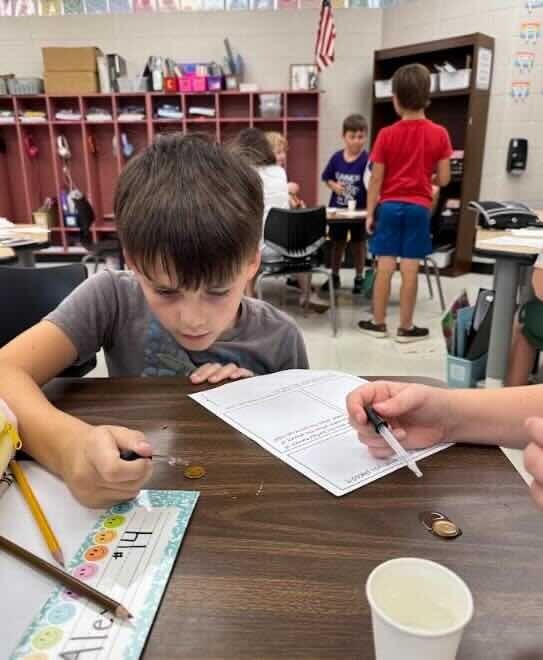 Student closely observes a penny while a classmate uses a dropper during a collaborative surface tension experiment.