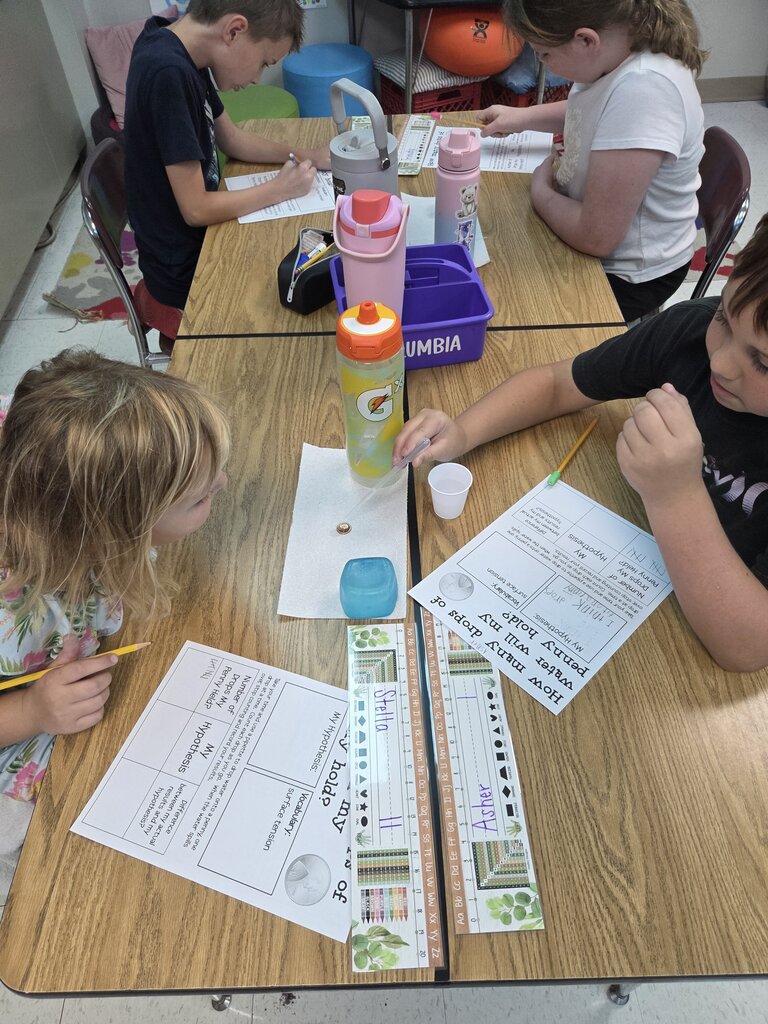 Students record observations and test water drops on a penny together during a hands-on classroom science activity.