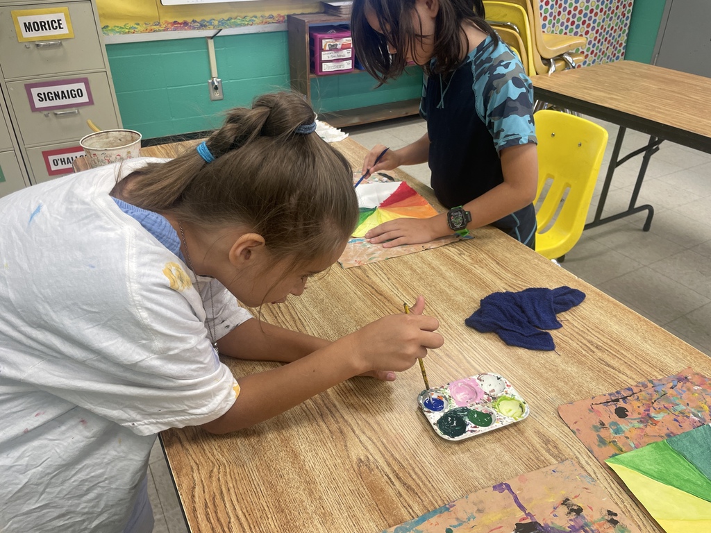 Two students carefully paint colorful sections of paper during an art activity at a classroom table.