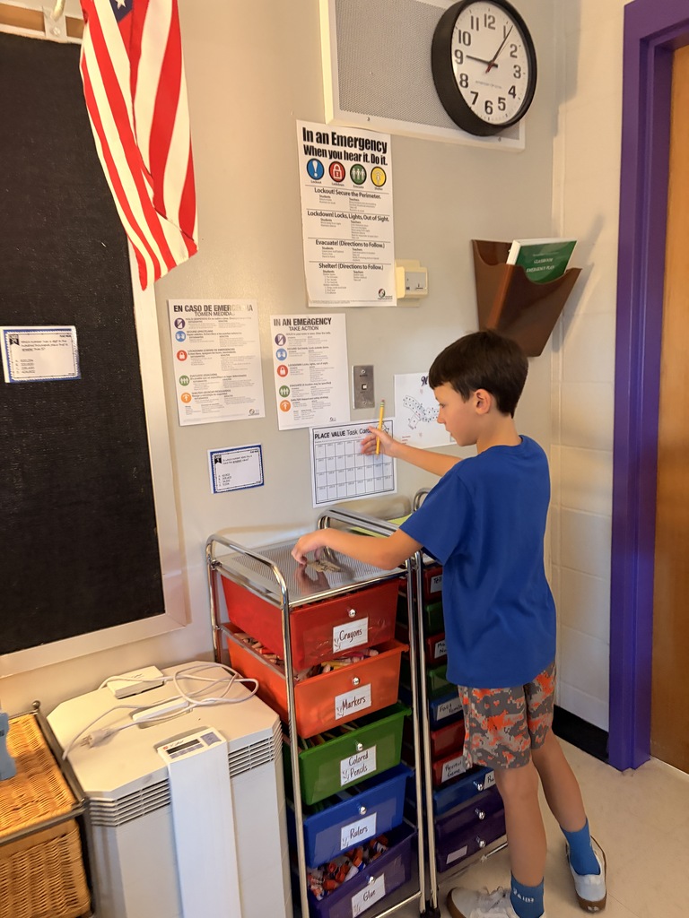 A student uses a pencil and classroom supply cart while completing a place-value task card activity.