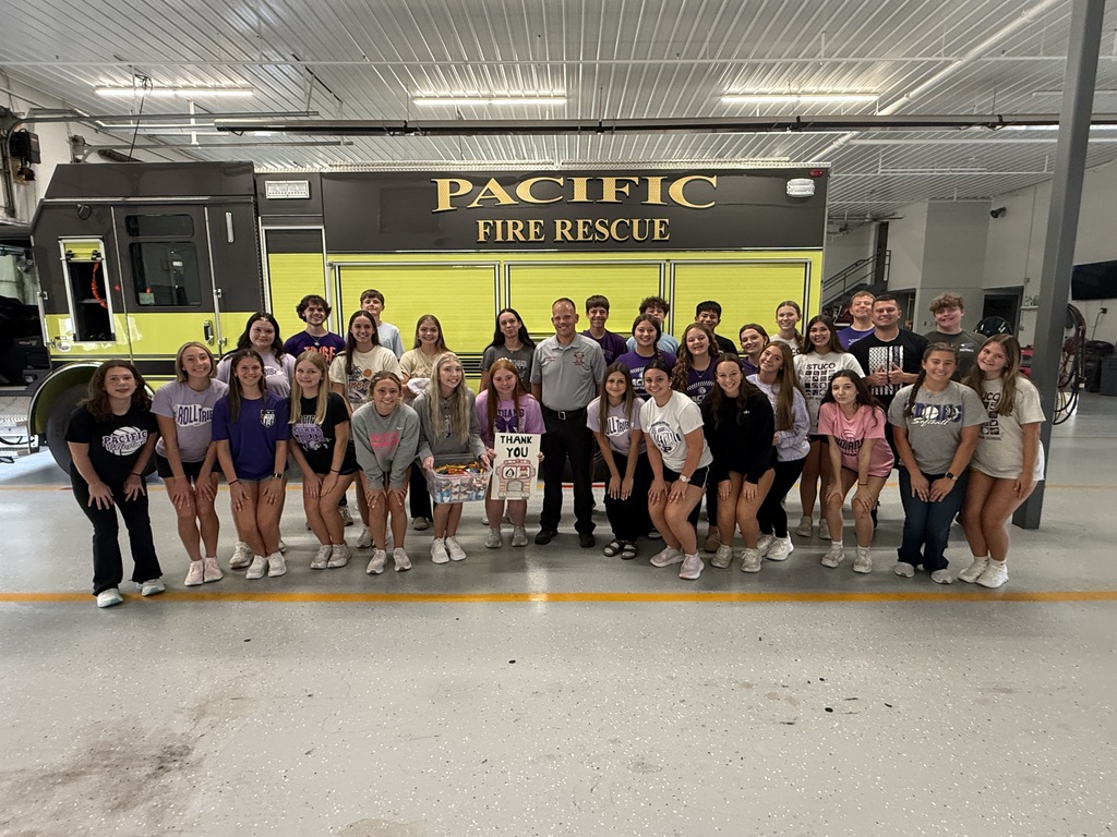 Students and firefighters pose together in front of a Pacific Fire Rescue truck, with a student holding a thank-you sign.