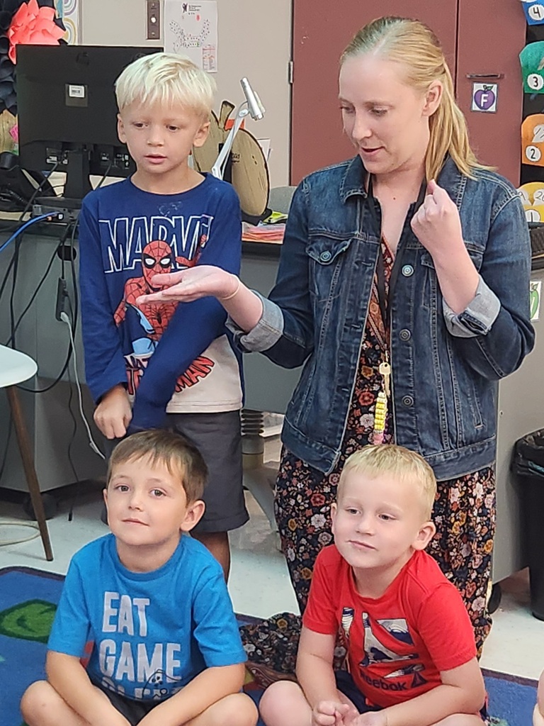 Teacher holds out her hand while three young students watch closely during a classroom activity.