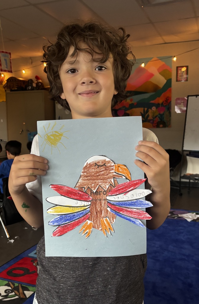 elementary students smile while holding colorful handmade bald eagle crafts featuring messages about heroes.