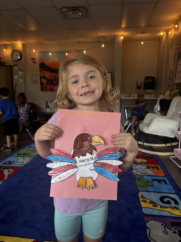 elementary students smile while holding colorful handmade bald eagle crafts featuring messages about heroes.