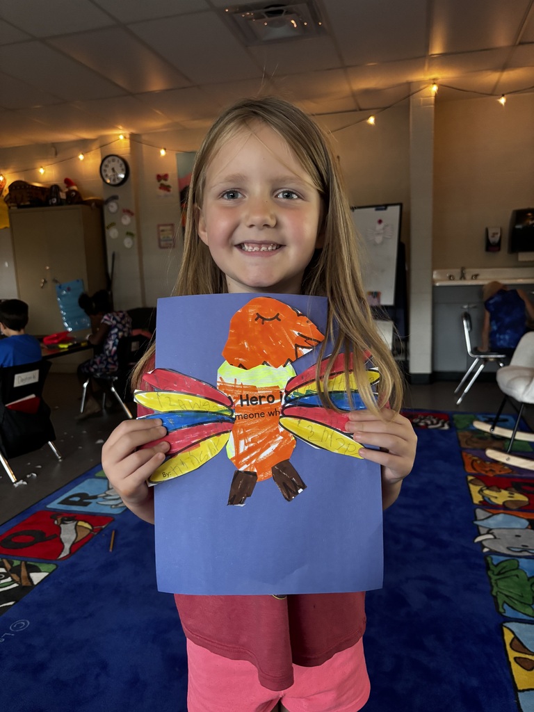 elementary students smile while holding colorful handmade bald eagle crafts featuring messages about heroes.