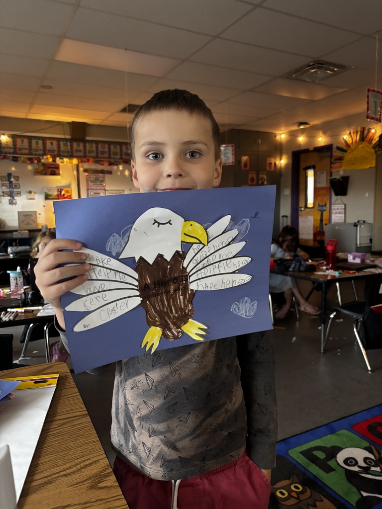 elementary students smile while holding colorful handmade bald eagle crafts featuring messages about heroes.