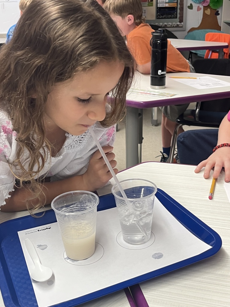 A student uses a straw to investigate liquids in two cups during a hands-on classroom science experiment.