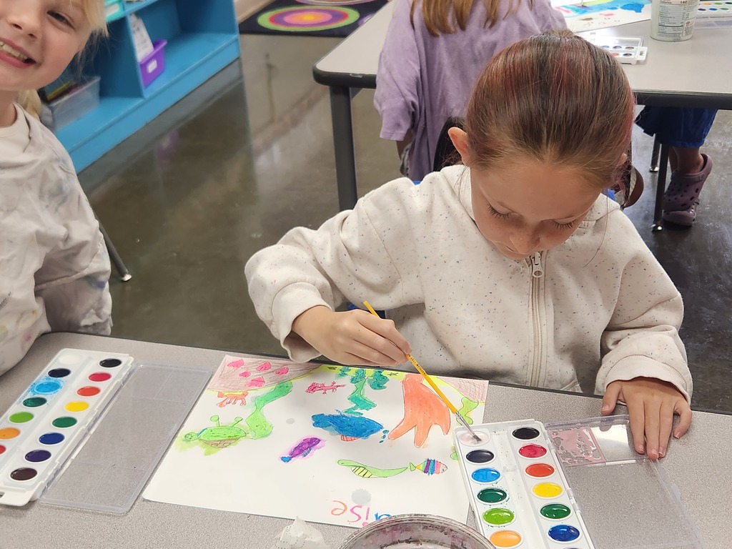 A student carefully adds watercolor details to a vibrant underwater scene filled with fish and sea life.