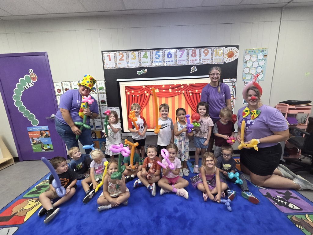 Preschoolers and teachers pose with colorful balloon animals and sculptures during a circus-themed classroom celebration.