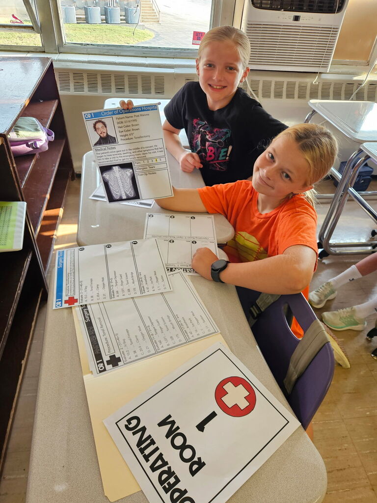 Two students smile while displaying a patient chart during a hospital-themed order of operations math lesson.