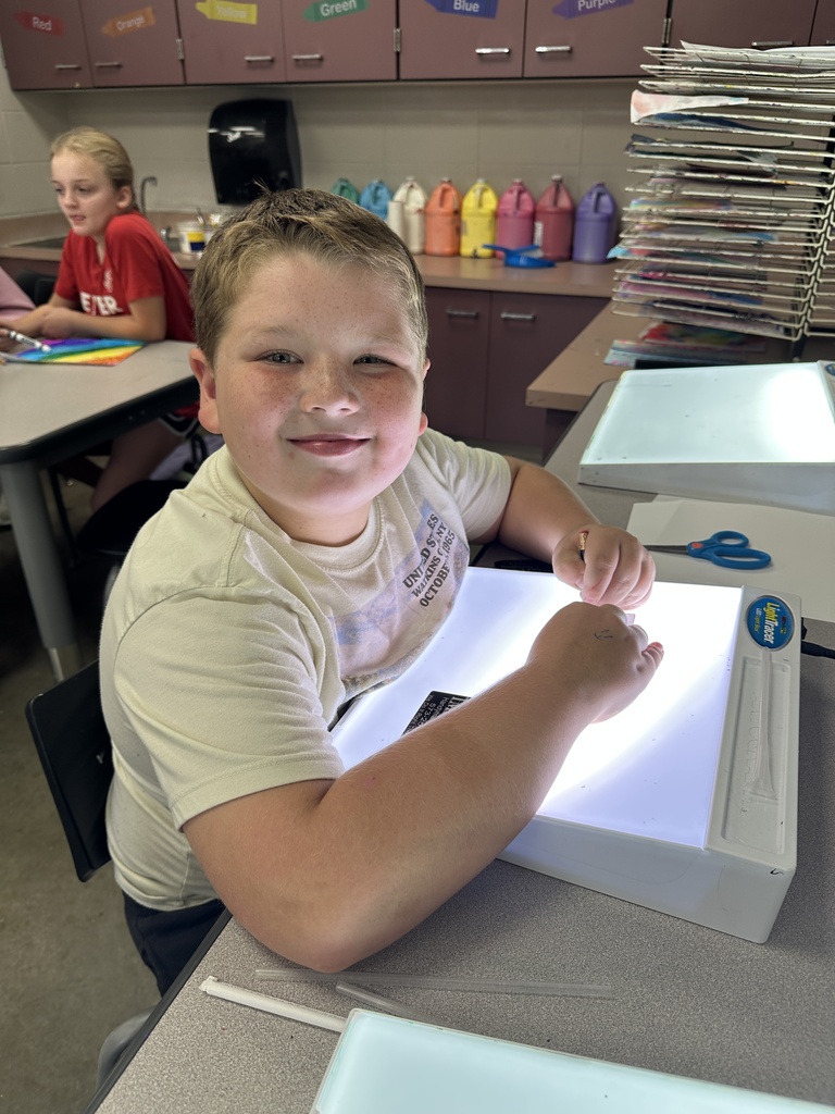 Student smiles while working at a glowing light table during an art classroom activity.