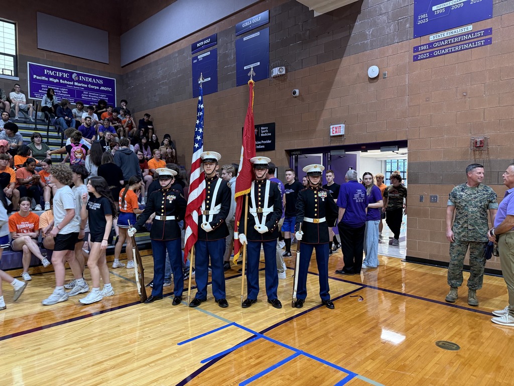 Marine Corps JROTC color guard presents the flags in a crowded school gym during a student assembly.