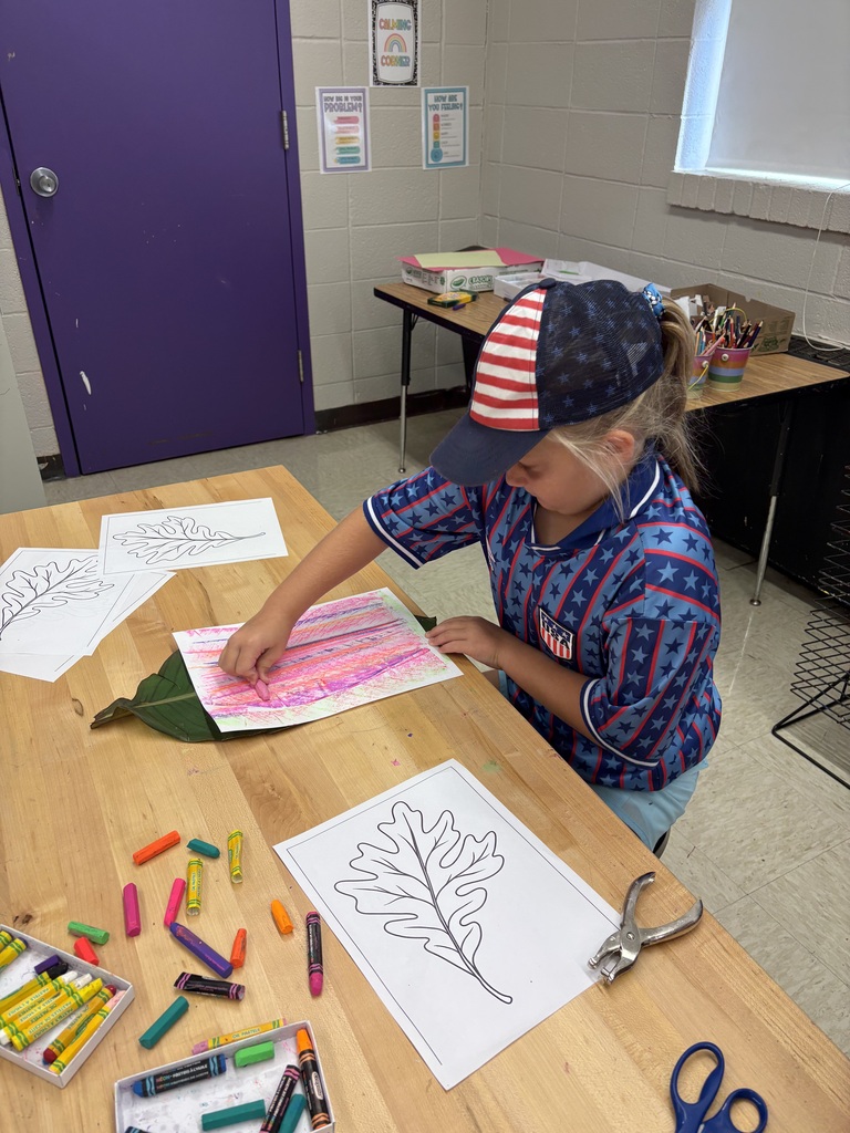 A student rubs colorful crayons over a leaf beneath paper, creating a textured leaf print during an art activity.