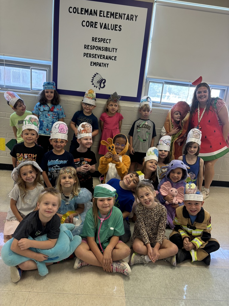 Coleman Elementary students and a teacher pose in colorful costumes and handmade hats beneath the school's core values poster.