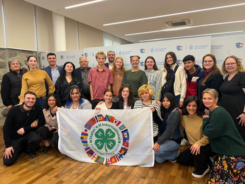 Students and adults pose together in Cรณrdoba, Argentina, holding a States' 4-H International Exchange Programs flag.