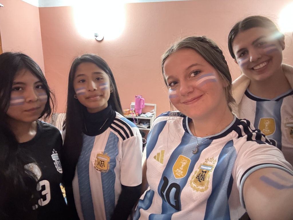 Four smiling students wearing Argentina soccer jerseys and blue-and-white face paint pose together for a selfie.
