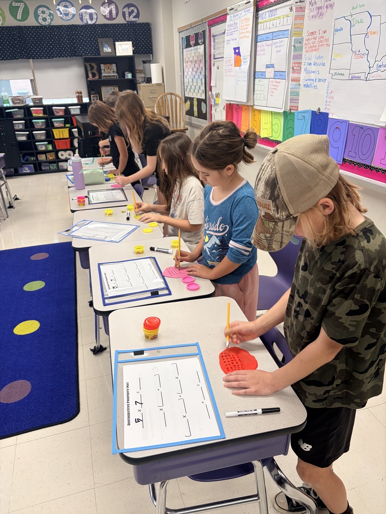 Elementary students use colorful modeling clay and pencils to practice multiplication and the distributive property at their desks.