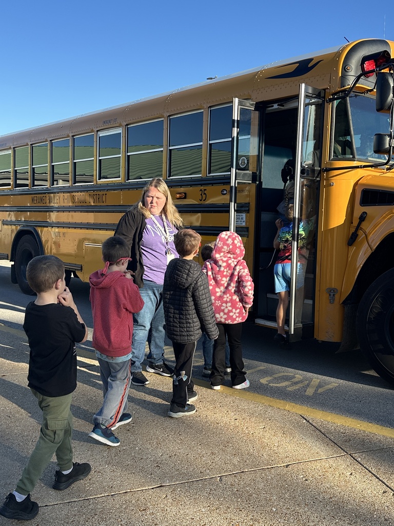 Students line up to board a yellow Meramec Valley R-III school bus as a staff member supervises on a sunny day.