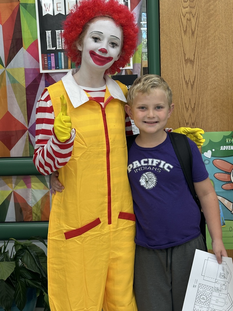 A student dressed as Ronald McDonald smiles beside a young boy wearing a purple Pacific Indians shirt.