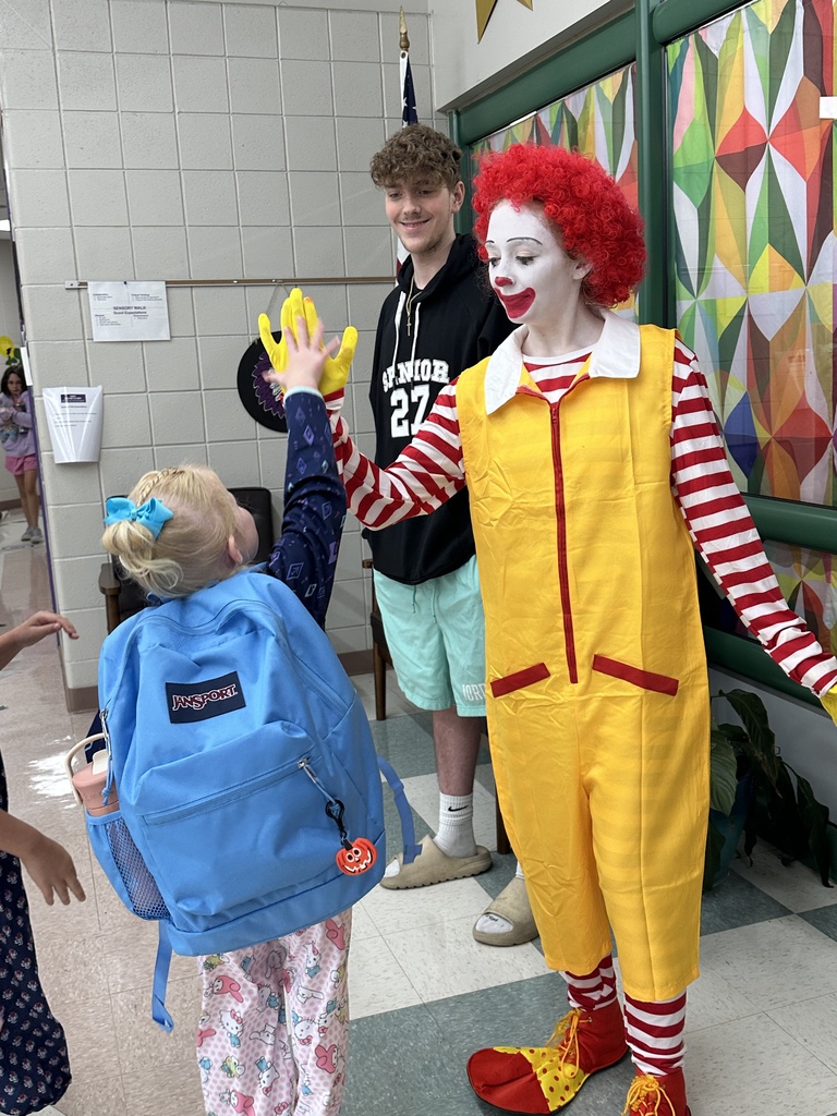 A young student wearing a blue backpack gives Ronald McDonald a high-five as an older student smiles nearby.
