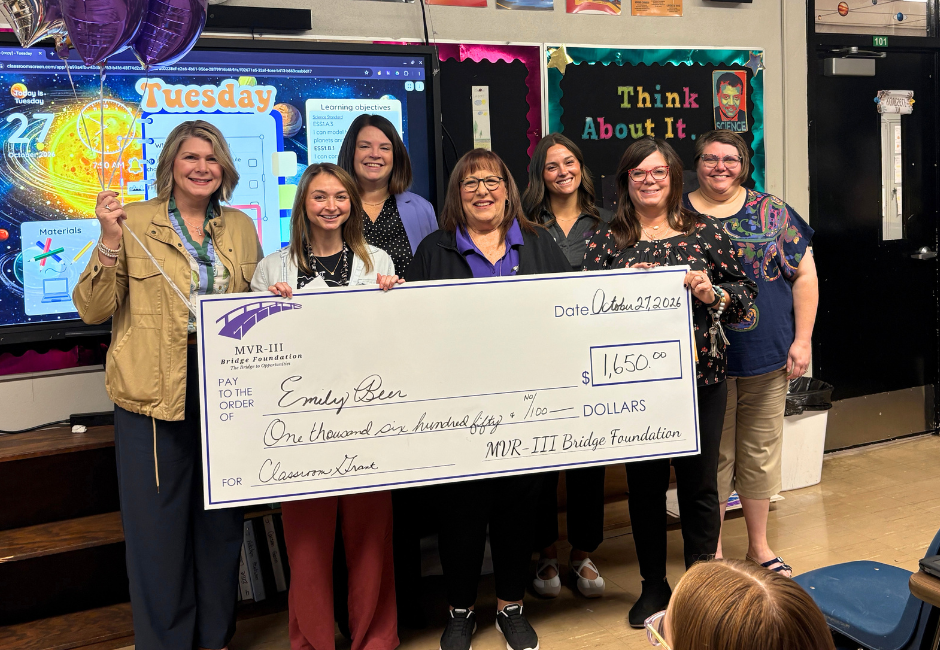 Various staff members pose with a large check in a school classroom.
