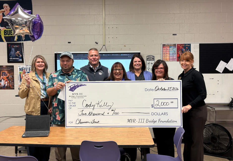 Various staff members pose with a large check in a school classroom.