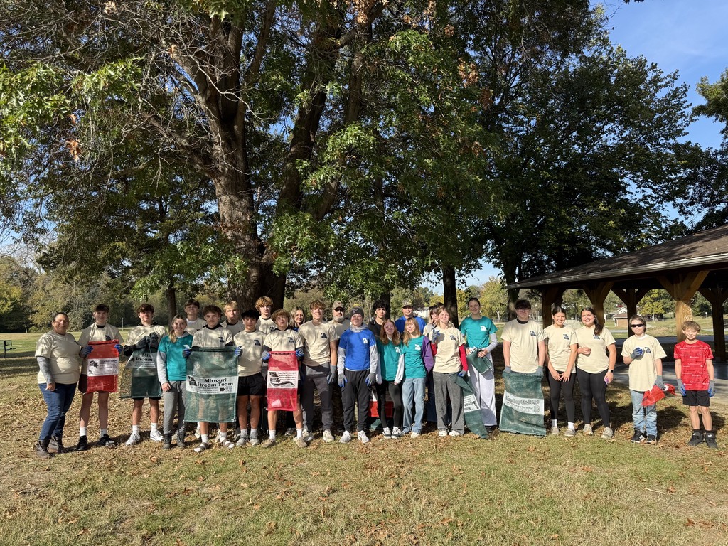 A large group of students stand outdoors posing with four banners.