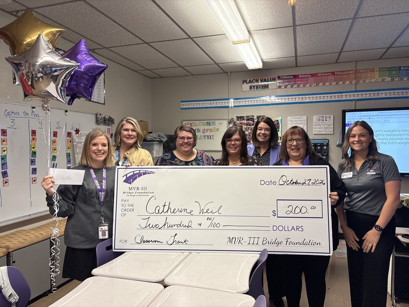 Various staff members holding a large check in a school classroom.
