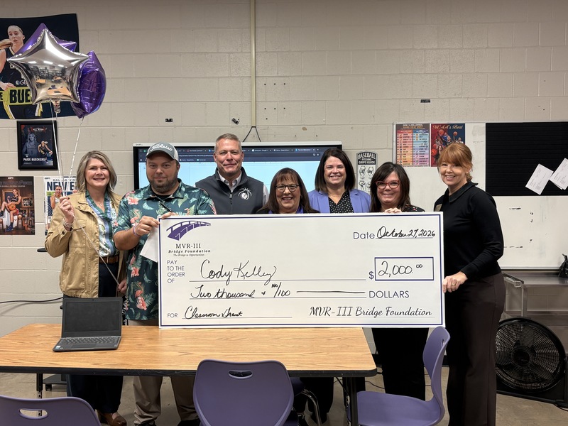 Various staff members holding a large check in a school classroom.