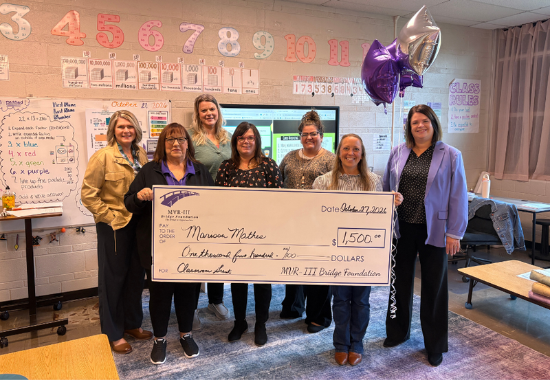 Various staff members holding a large check in a school classroom.
