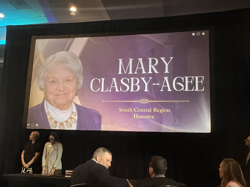 Large event screen displays a portrait and the name Mary Clasby-Agee, labeled South Central Region honoree, above seated attendees.