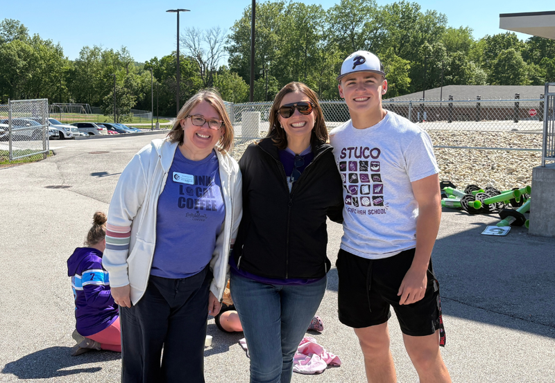 Two staff members pose with a student outside.