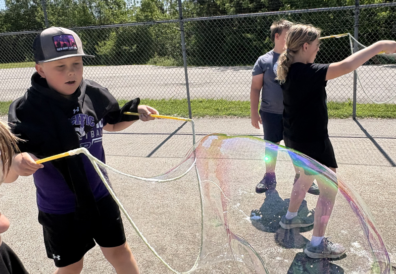 Three students playing with bubbles outside.