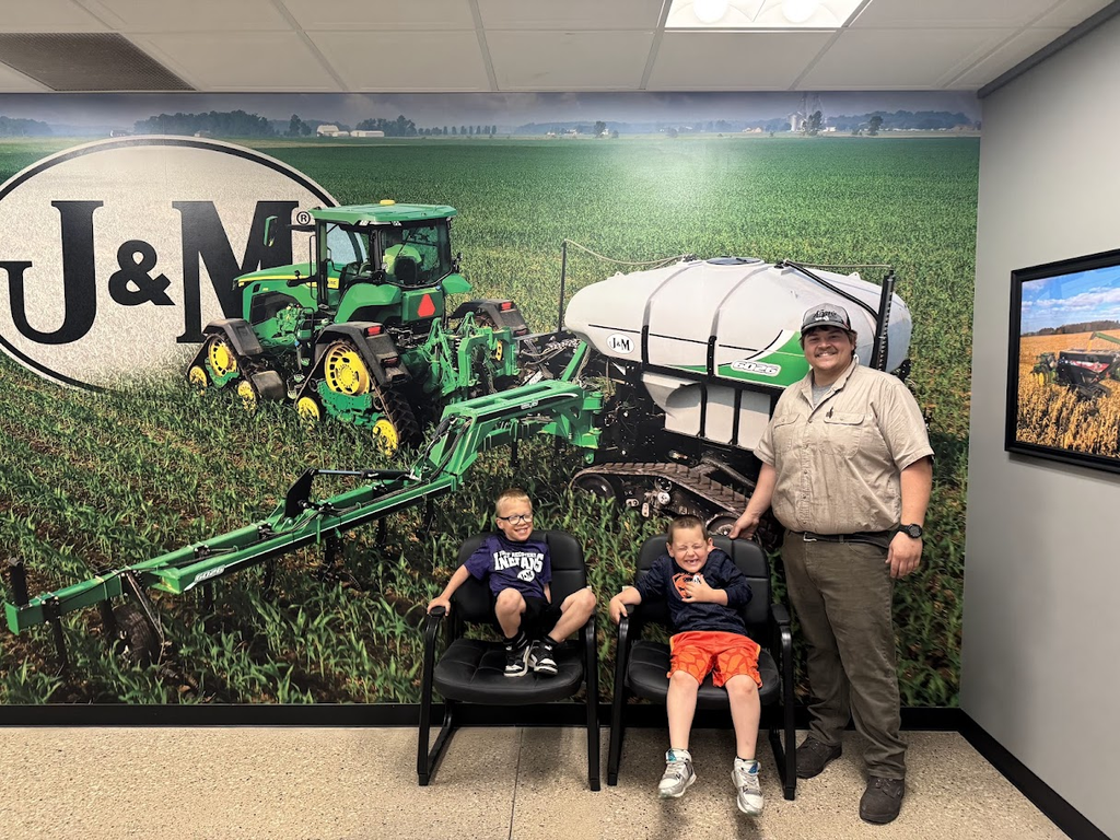 A man stands with two children in front of a wall mural featuring farm equipment.
