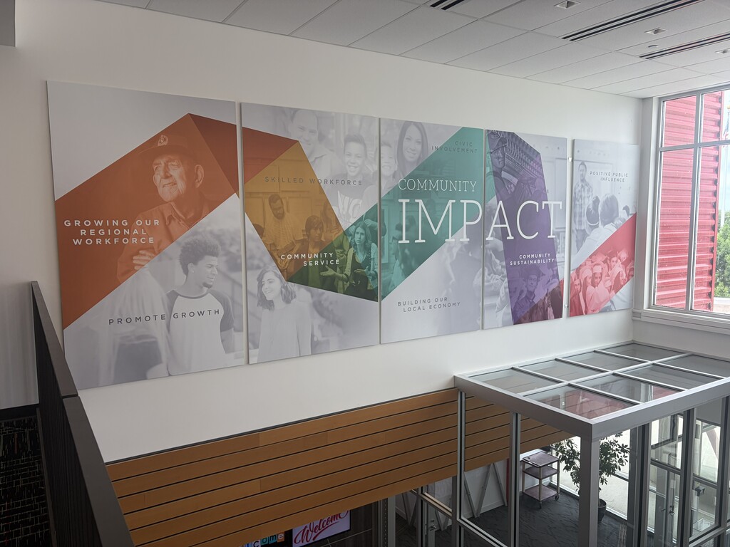 Interior of a building with three large wall panels displaying images of people and text reading "IMPACT" on a white wall.