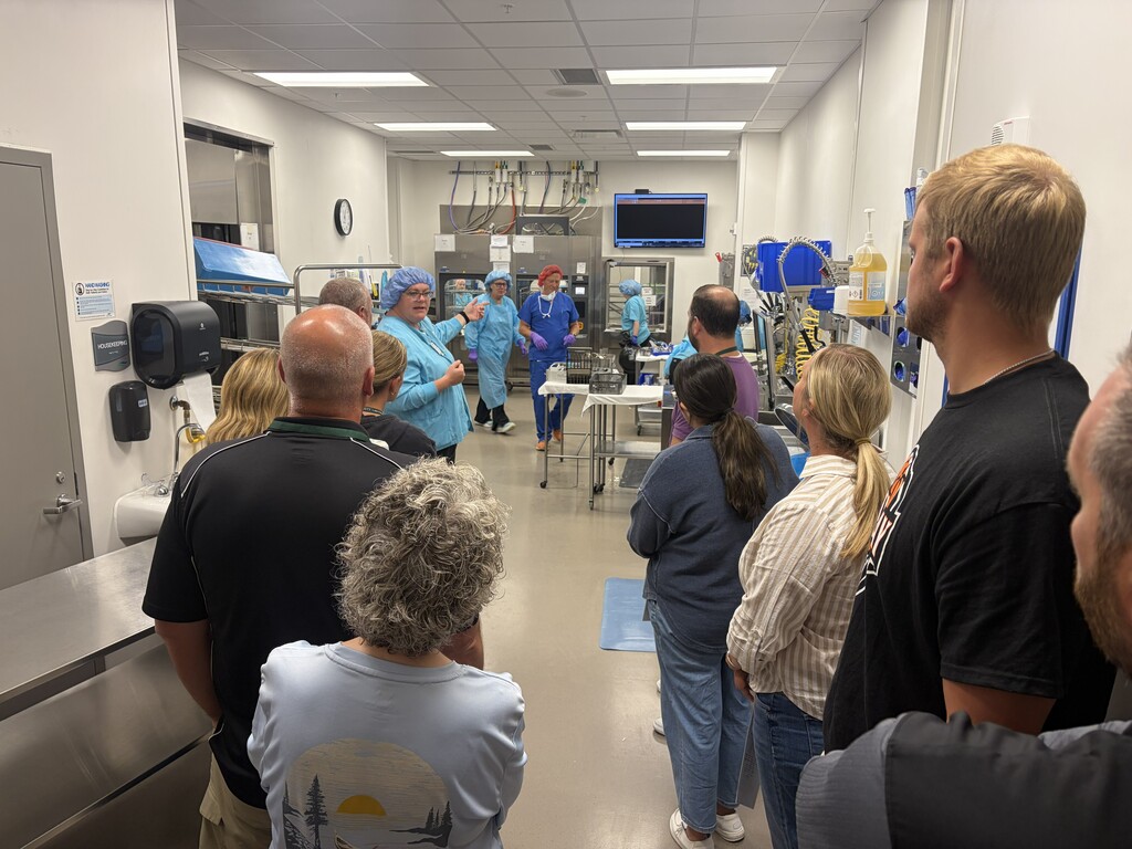 A hospital hallway with white walls has a group of people in scrubs and lab coats.