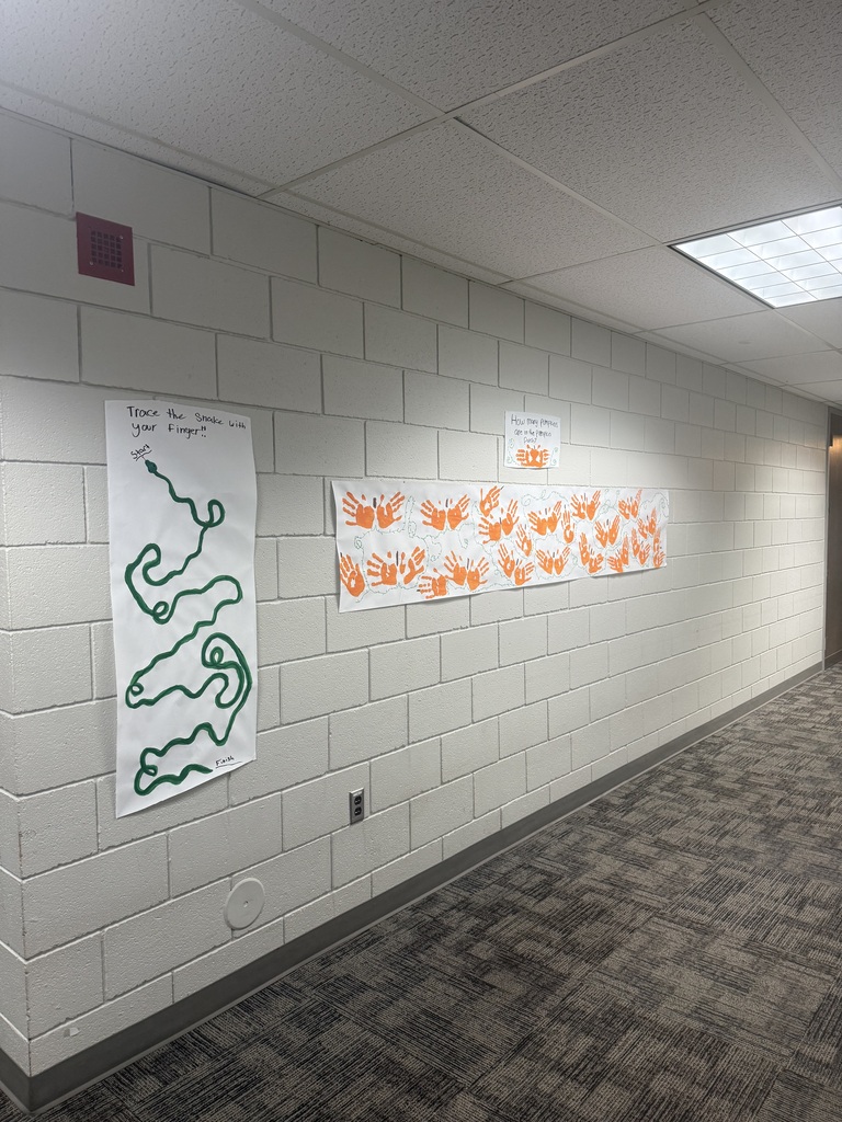 Empty hallway with white brick walls and two posters. One poster has green drawings; the other has orange handprints.