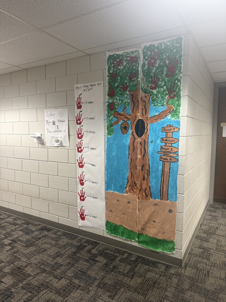 An empty hallway with a tree mural and a sign. The tree has apples, a hollow trunk, and a birdhouse.